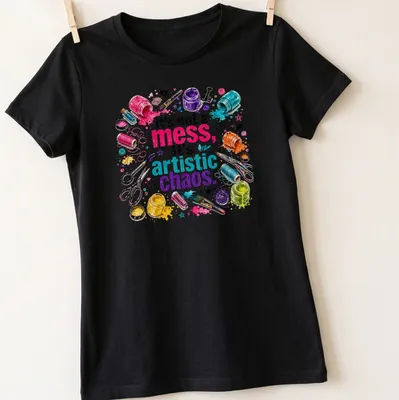 Colorful watercolor print featuring crafting supplies and the phrase 'It's not a mess, it's artistic chaos.' — printed on a women's shirt
