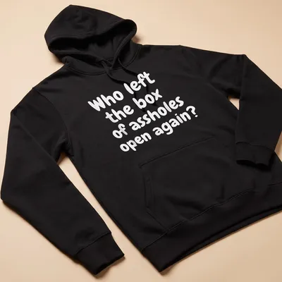Funny T-shirt with text asking who left the box of assholes open again, against a white background. — printed on a unisex hoodie