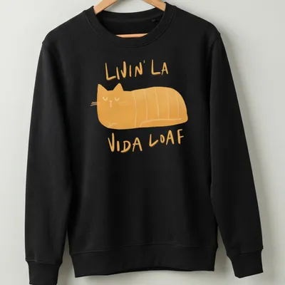 Kawaii illustration of a loafing cat with text 'Livin' La Vida Loaf' in orange and cream. — printed on a unisex sweatshirt