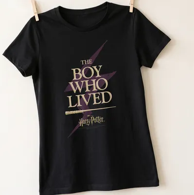 Bold lettering of 'The Boy Who Lived' with a lightning bolt motif in gold and purple — printed on a women's shirt