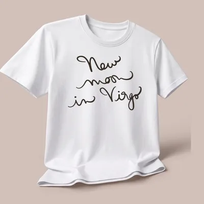 Handwritten script design reading 'New moon in Virgo' in black text — printed on a unisex t-shirt (angled view)