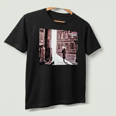 Vintage style shirt featuring a person in a trench coat labeled 'camel stationary traveller' — printed on a unisex t-shirt (angled view)