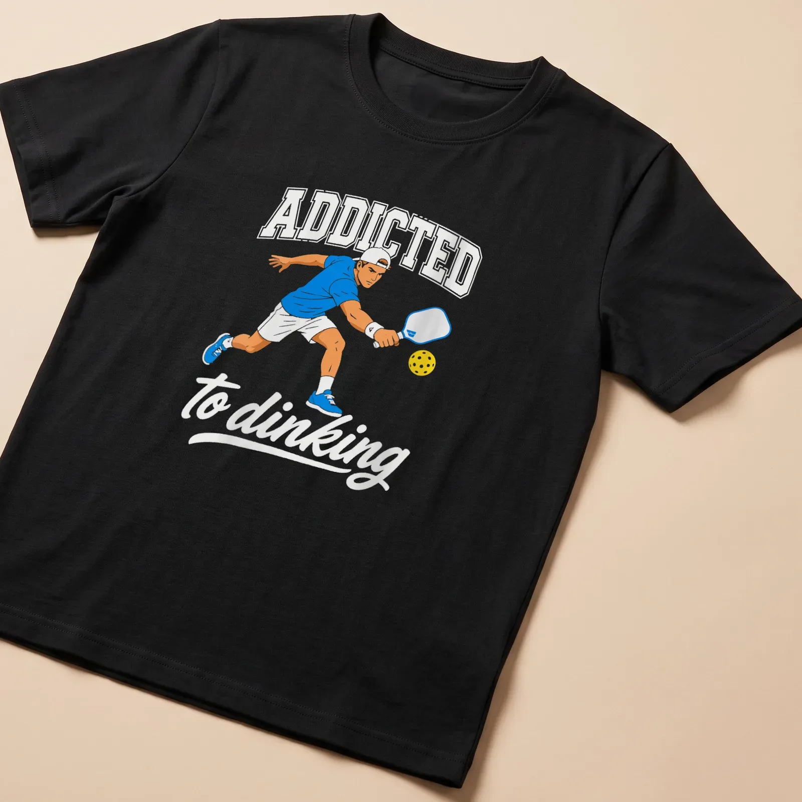 Bold printed text 'ADDICTED to dinking' with a Pickleball player design — printed on a unisex t-shirt