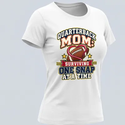 Bold, colorful text reads 'Quarterback Mom: Surviving One Snap at a Time' with football imagery — printed on a women's shirt