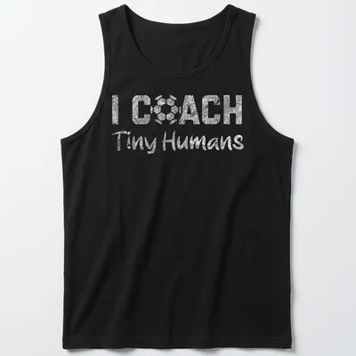 Bold playful text 'I COACH Tiny Humans' on a black and white soccer-themed — printed on a tank top