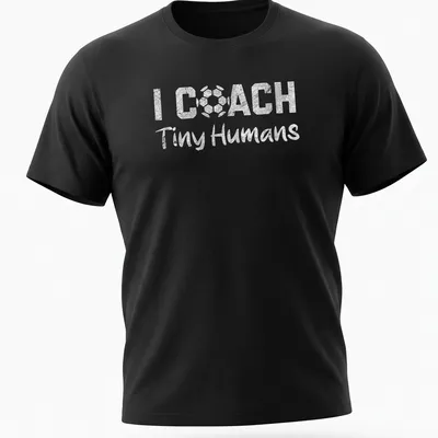 Bold playful text 'I COACH Tiny Humans' on a black and white soccer-themed shirt
