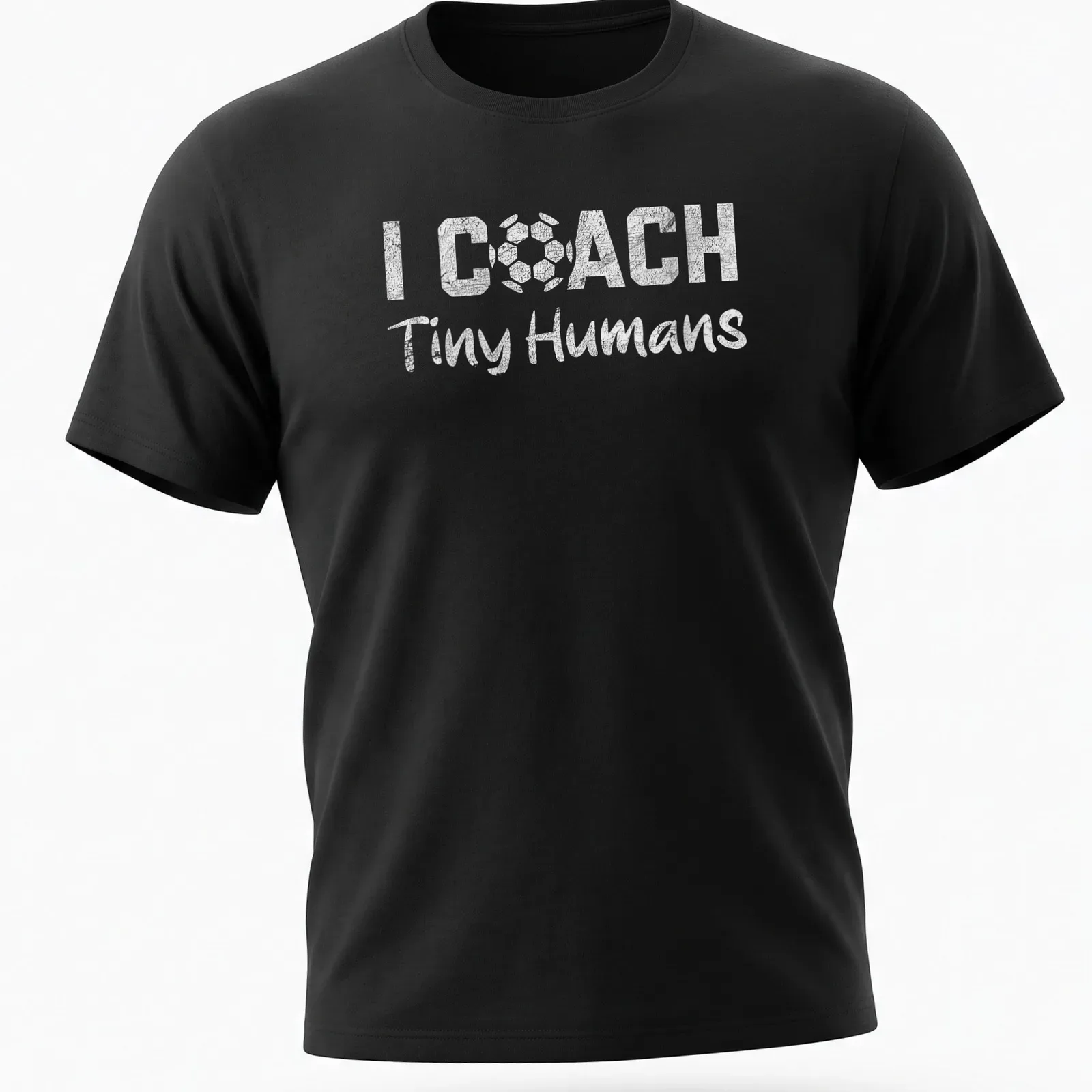 Bold playful text 'I COACH Tiny Humans' on a black and white soccer-themed — printed on a unisex t-shirt