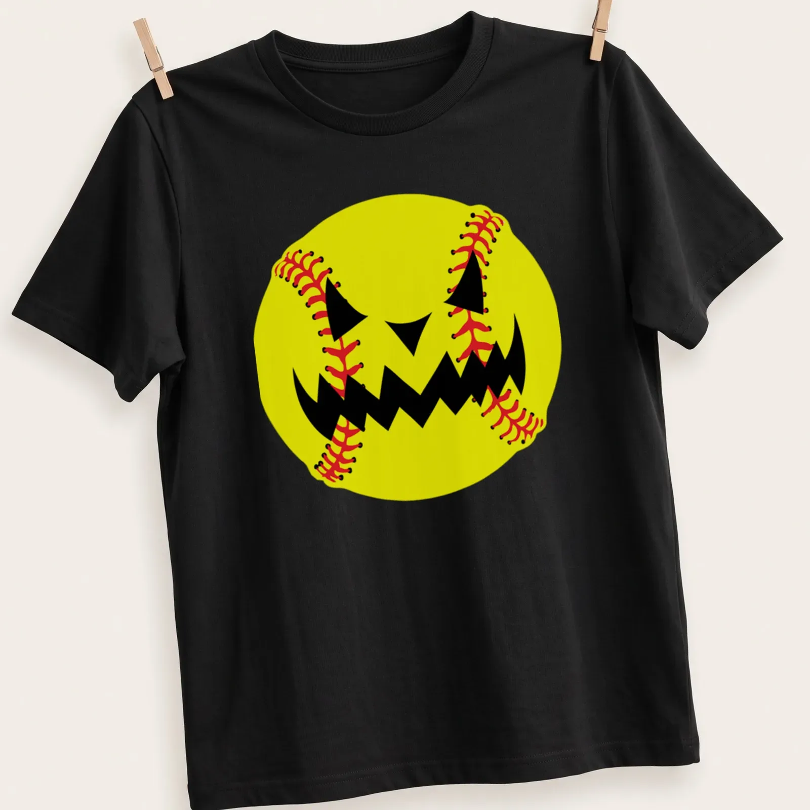 Cartoon pumpkin jack-o'-lantern face resembling a softball in yellow, black, and red — printed on a unisex t-shirt
