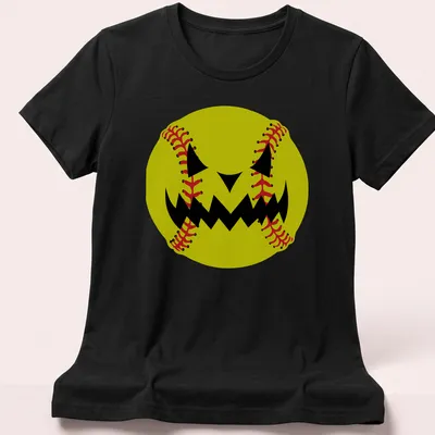 Cartoon pumpkin jack-o'-lantern face resembling a softball in yellow, black, and red — printed on a women's shirt